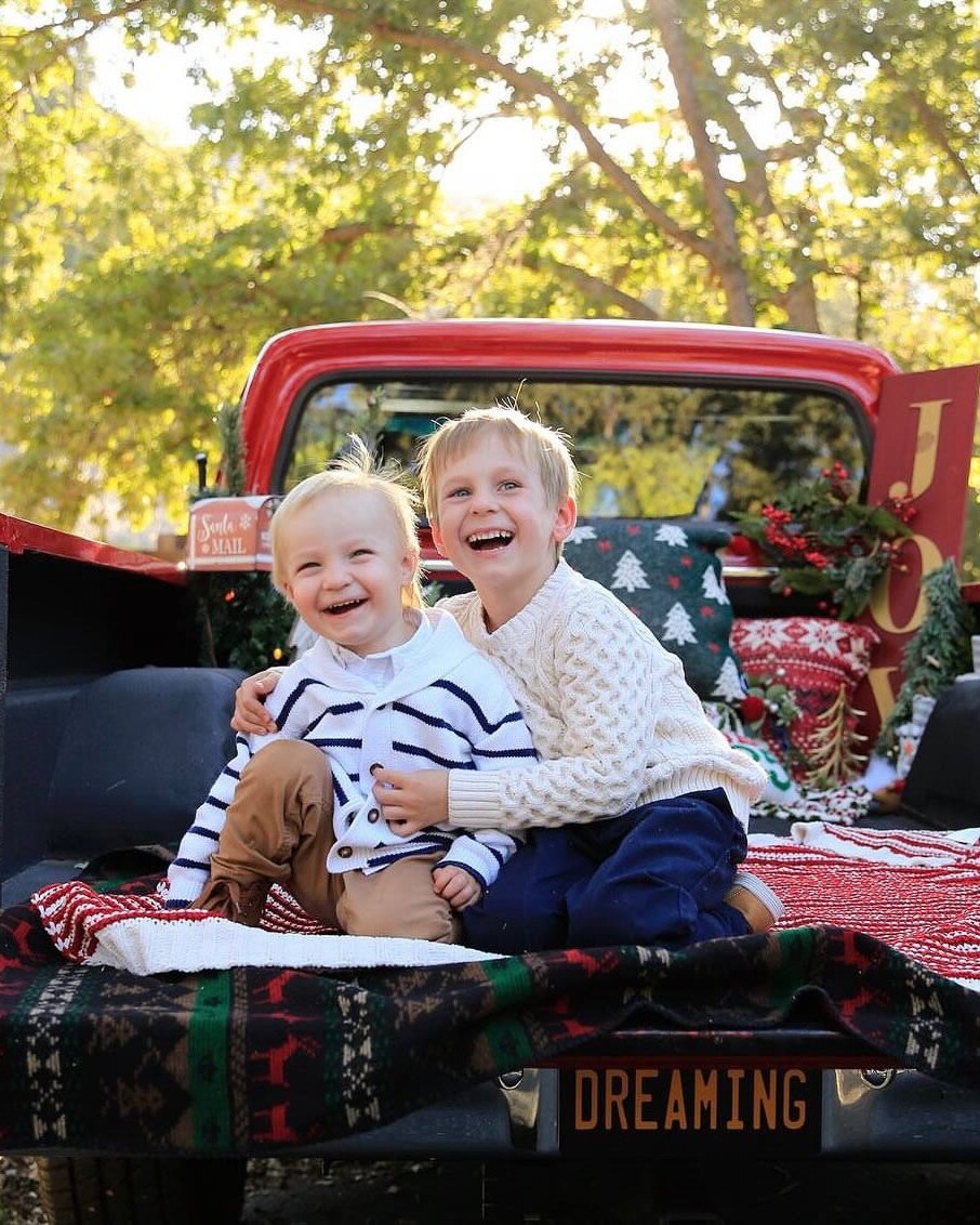 Two young brothers laughing in the bed of the red 1972 Ford F-100, decorated with a JOY sign and holiday blankets.