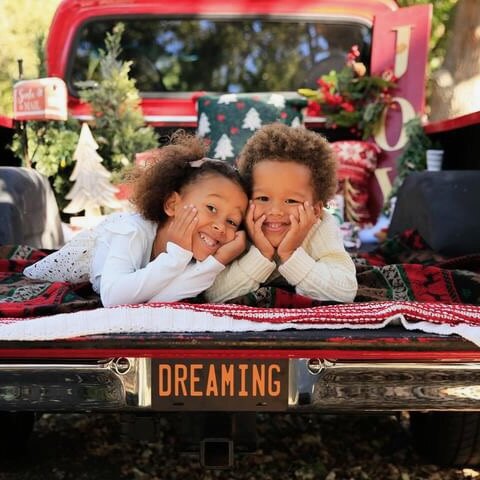 Two children resting on the tailgate of the red 1972 Ford F-100 among holiday blankets.