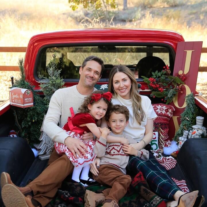 A family of four seated in the bed of the red 1972 Ford F-100, surrounded by holiday decorations.