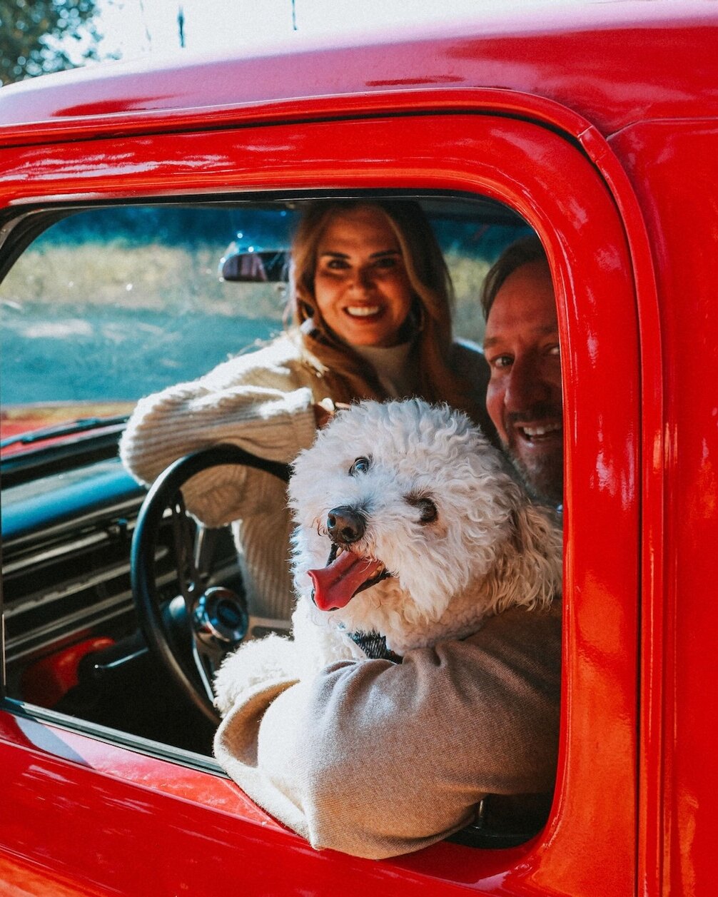 A couple and their dog looking out through the open driver's window of the red 1972 Ford F-100.
